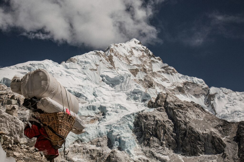 Un porteur himalayan transportant une charge massive sur un sentier de montagne escarpé