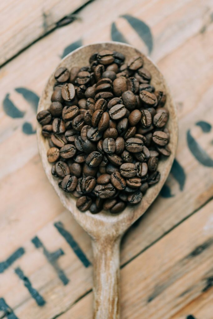 Grains de café torréfiés dans une cuillère en bois, symbolisant l'origine et la qualité du café de spécialité