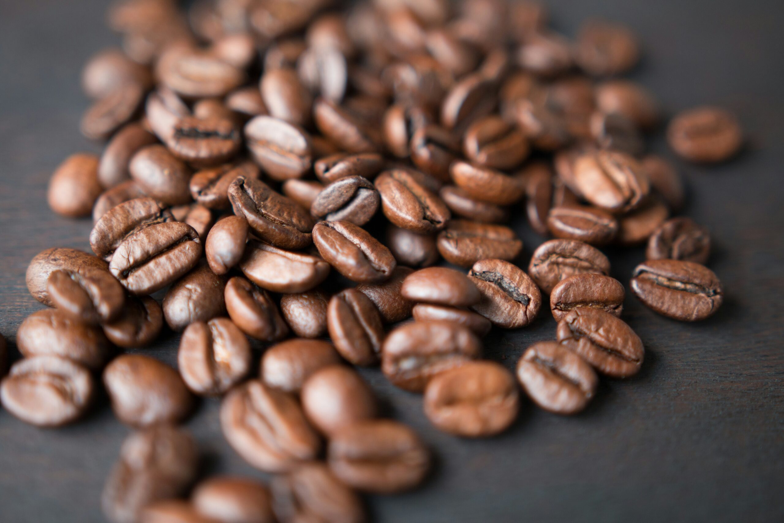 Grains de café torréfiés dispersés sur une surface sombre, illustrant l'excellence du café de spécialité