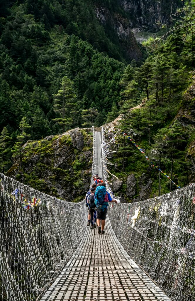Trekkeurs traversant un pont suspendu orné de drapeaux de prière en forêt himalayenne