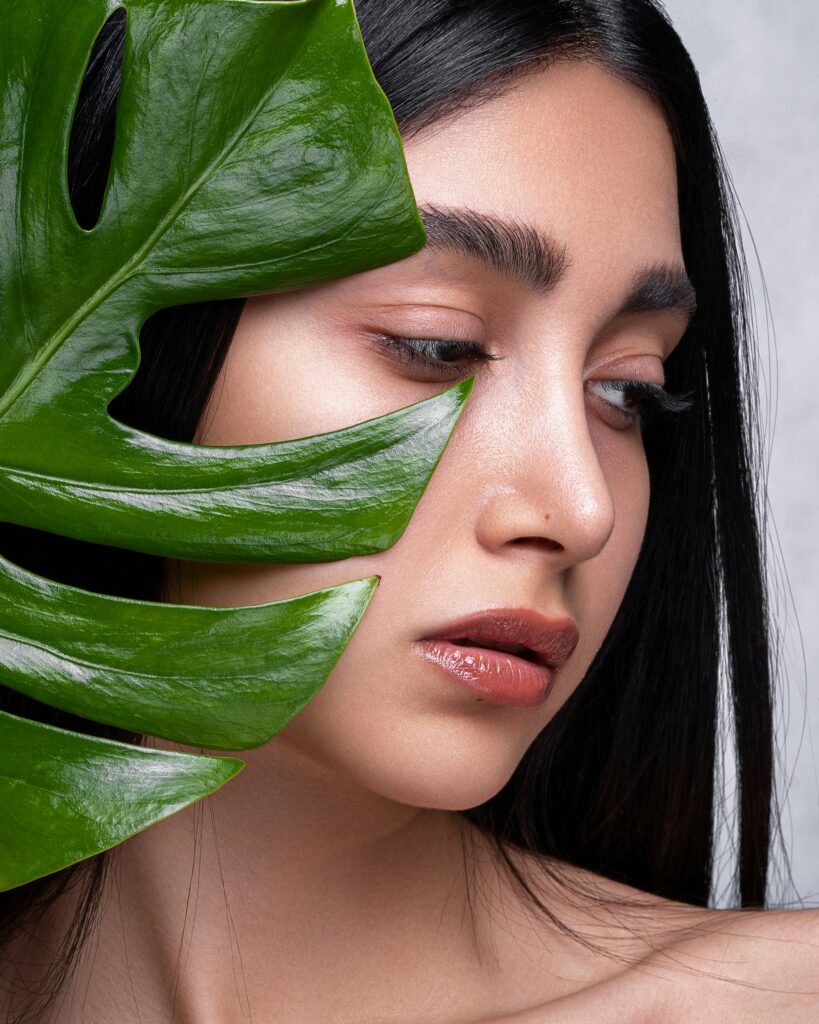 Portrait en gros plan d'une femme avec une feuille de monstera verte, illustrant la beauté naturelle au cœur de la philosophie Nūde